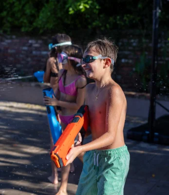 Three kids laughing while holding water guns at a water gun party