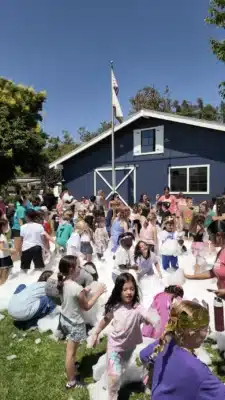 group of kids playing in foam in front of a blue building on a grass field