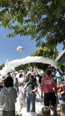 group of kids playing in a foam party with a green foam machine.