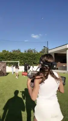 teen dressed in white holding a laser tag with teens in the background in a backyard with green grass